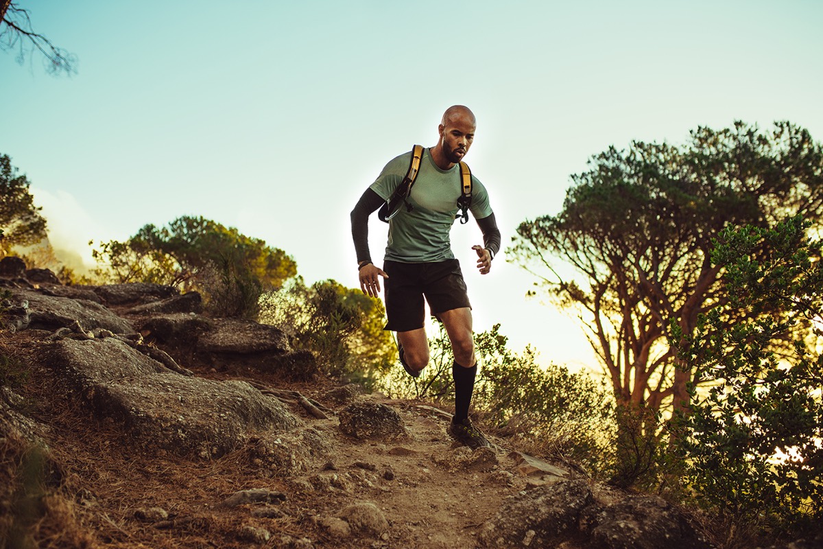 A trail runner with a hydration pack running down a rocky hillside path at sunset
